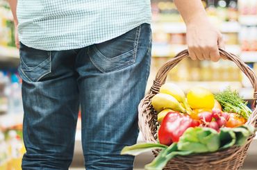 Mann trägt Korb mit frischem Gemüse und frischen Früchten