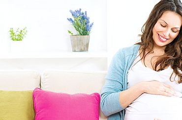 Frau sitzt auf dem Sofa und hält ihren Schwangerschaftsbauch