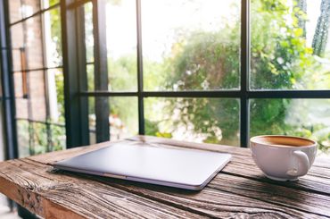 Kaffee und Laptop stehen auf dem Tisch vor dem Fenster