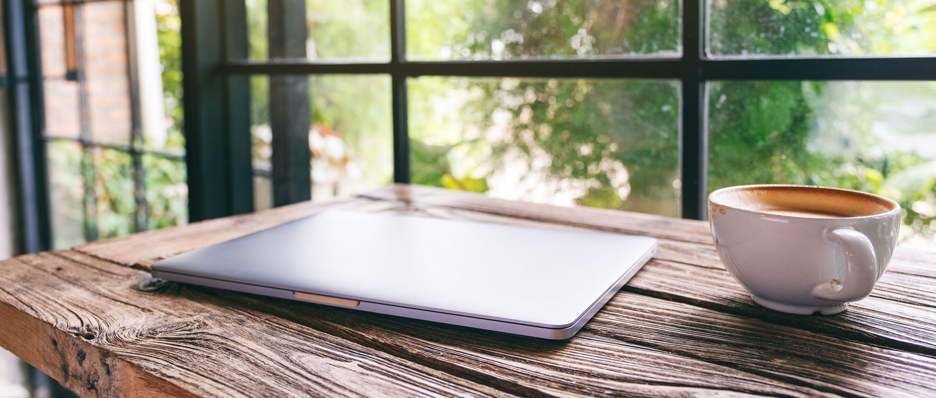 Kaffee und Laptop stehen auf dem Tisch vor dem Fenster