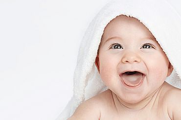 Lachendes Baby schaut unter dem Badetuch hervor