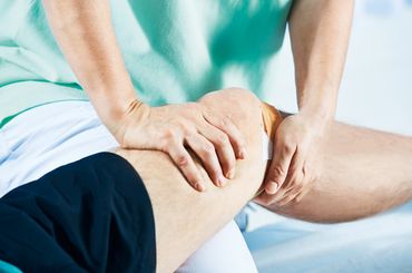 Physiotherapeutin behandelt Knie eines Patienten