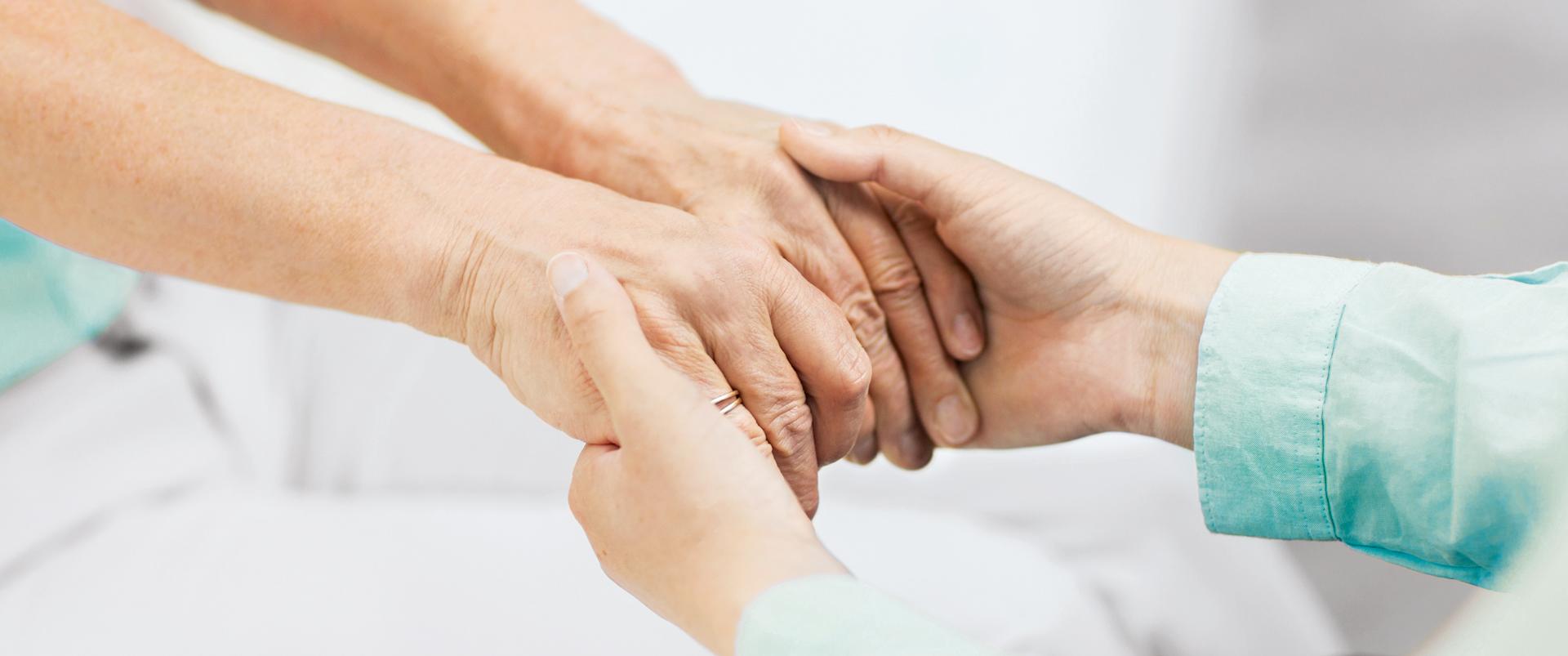 Patientin hält die Hände einer Betreuungsperson
