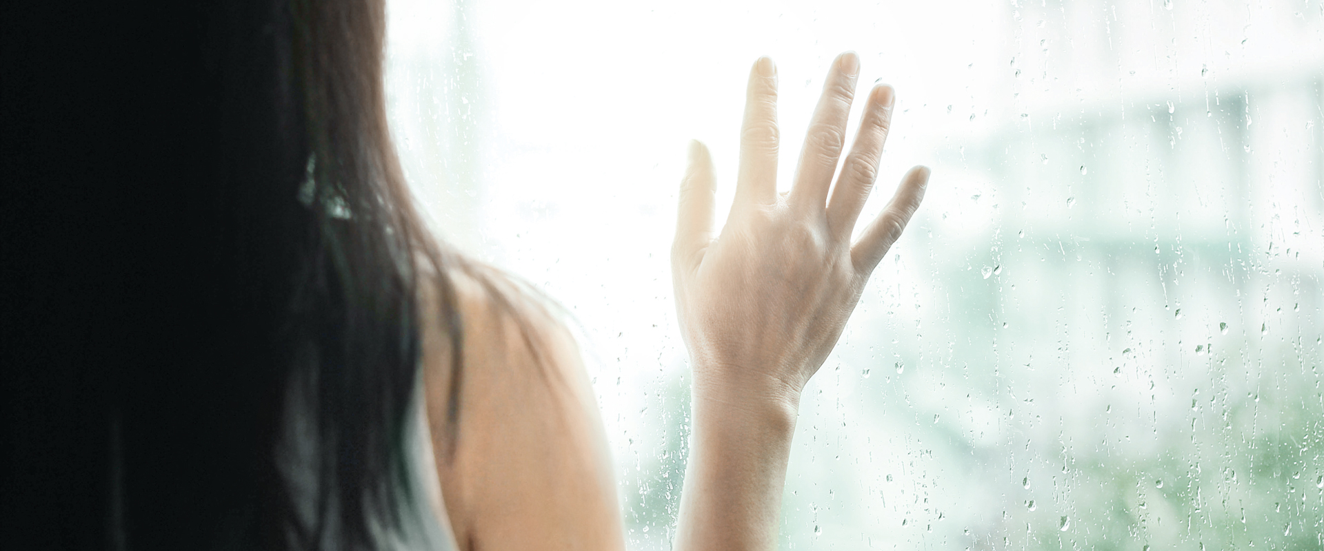 Frau schaut aus dem Fenster in den Regen